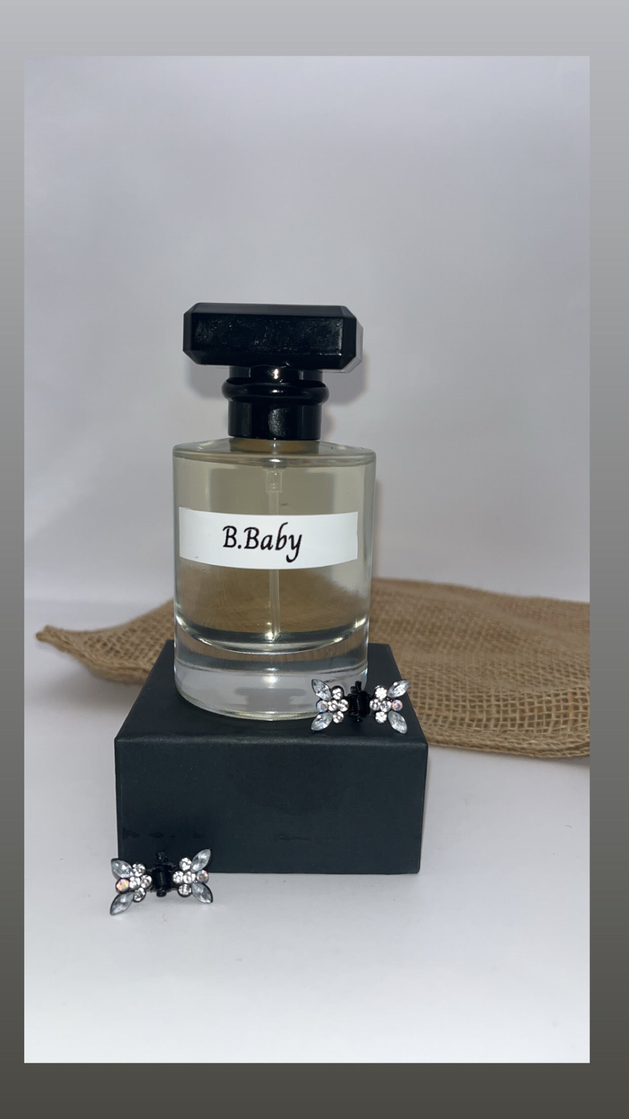 Perfume bottle labeled 'B.Baby' with a black base and silver earrings on a white background