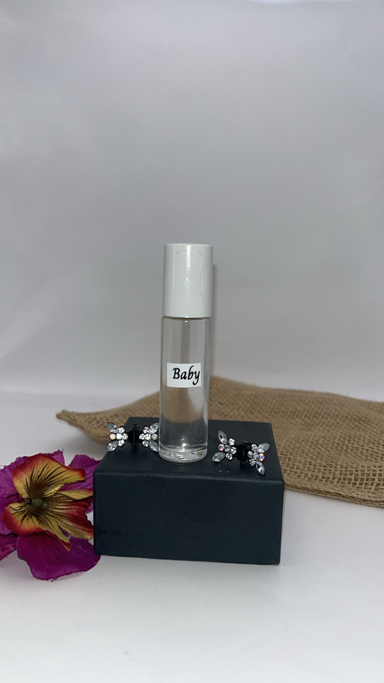 Small perfume bottle labeled 'Baby' on a black stand with a white background