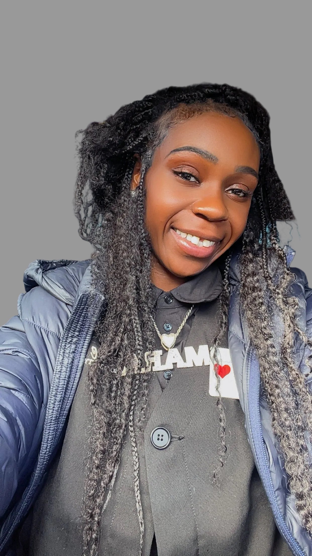 Woman with braided hair sitting inside a vehicle, wearing a gray jacket and a heart-shaped pendant. deep wave hair texture is popping!